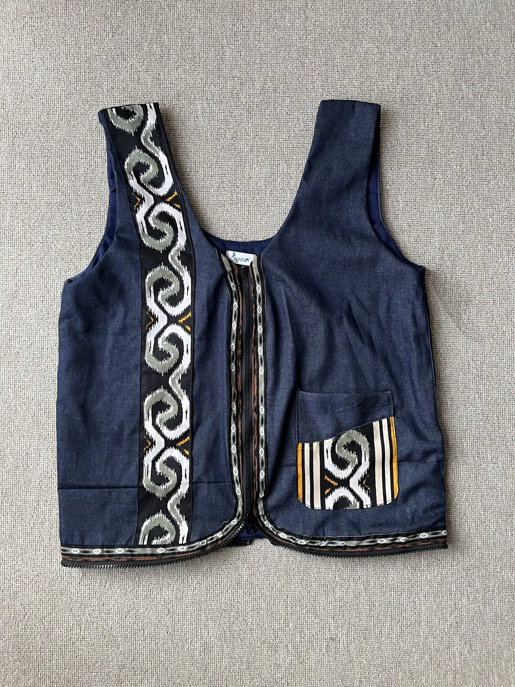 Vest denim navy Seri Jantra dengan panel tenun ikat motif pilin hitam-putih dan saku dada, tampak depan