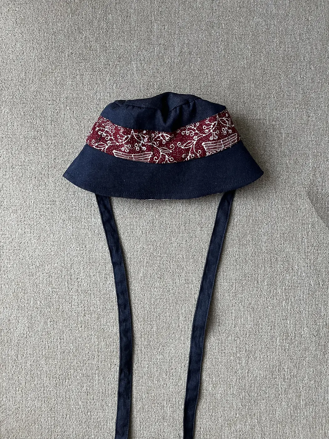 Bucket hat denim navy Seri Laras dengan band batik maroon bermotif flora dan tali panjang