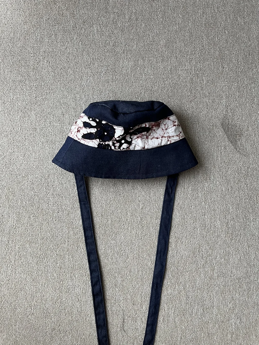 Bucket hat denim navy Seri Savitri dengan band batik remukan putih-cokelat dan aplikasi motif daun hitam serta tali panjang denim